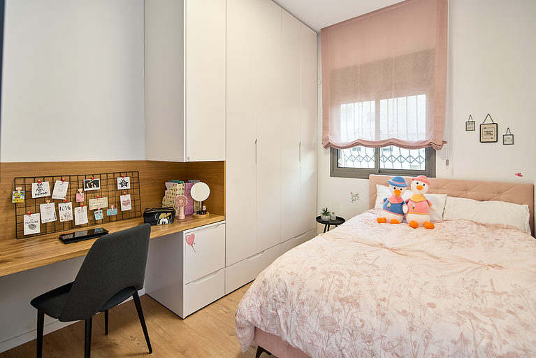 חדר שינה של ילדה בכפר סבא עם מיטה מרופדת ורודה, וילון רומי תואם, רצפת פרקט אלון, וארון משולב שולחן עבודה בהתאמה אישית בגימור צבע ופורניר אלון.