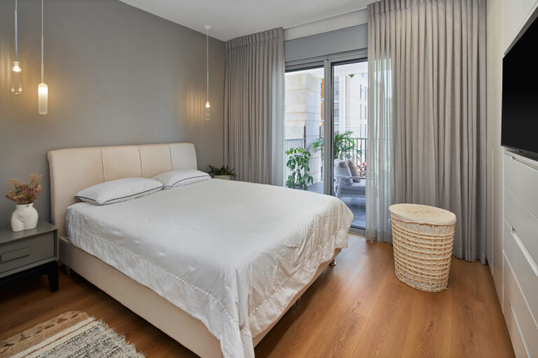 חדר שינה עם מיטה מרופדת בהירה, רצפת פרקט, קיר כוח מאחורי המיטה, תאורה תלויה ושידות צד מיטה, בעיצוב פנים מאת ענבל חן אדריכלות ועיצוב פנים בגליל ים, הרצליה.