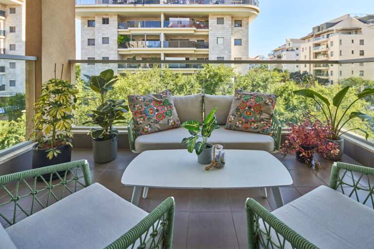 מרפסת עם פינת ישיבה, צמחייה ירוקה וכריות צבעוניות בפרויקט עיצוב דירה בכפר סבא.