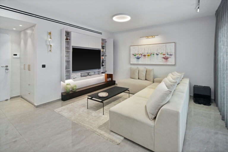 דירה מקבלן בגני תקווה – עיצוב סלון מודרני. סלון מודרני עם ספה בהירה, שולחן שחור, אמנות קיר צבעונית ווילונות שקופים